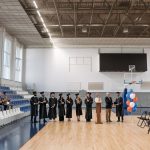A graduation ceremony held in an indoor gymnasium with graduates and an audience.